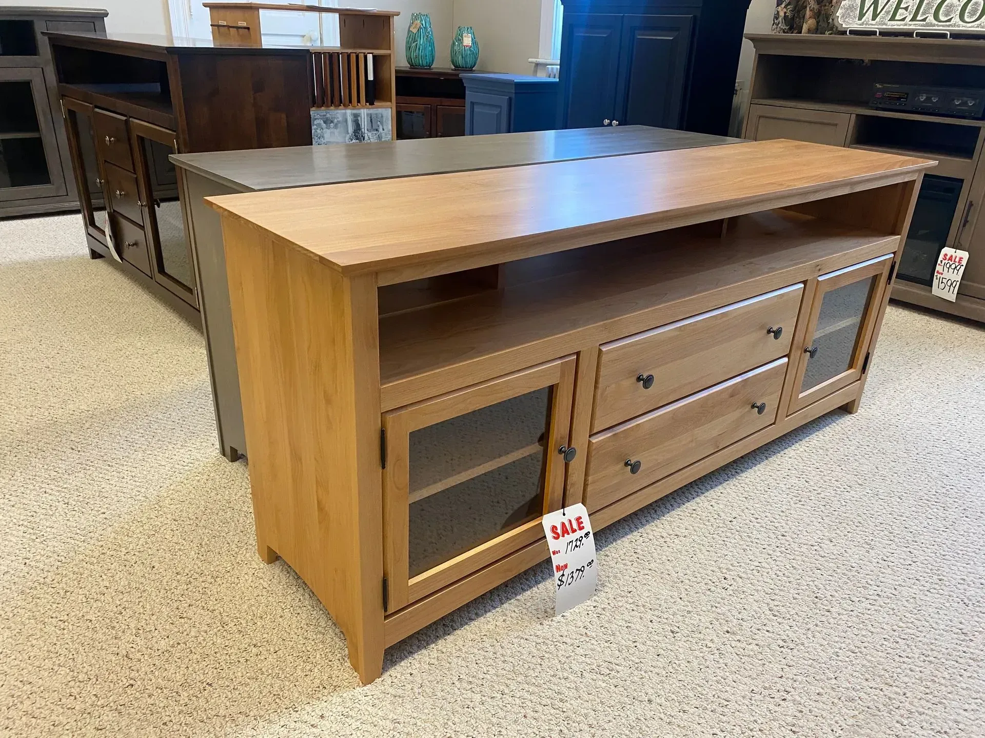 Wooden TV console with glass doors and drawers. Brown furniture in a showroom setting.