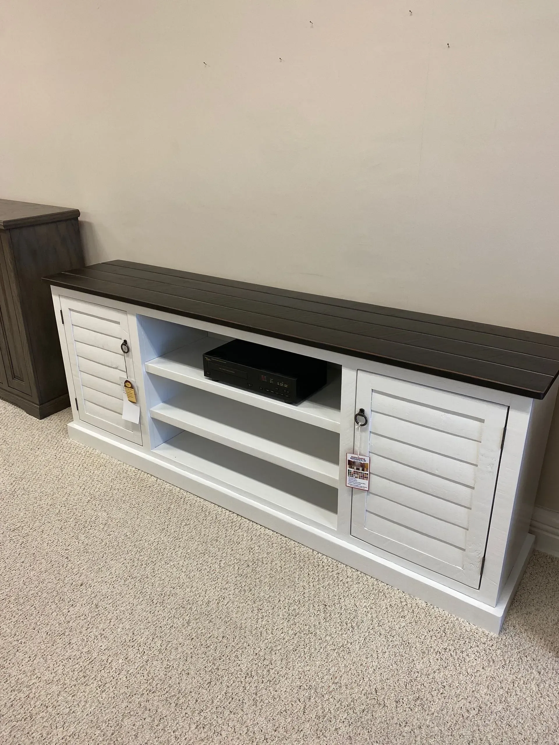 White and black TV stand with shutter doors and open shelves, on carpet.