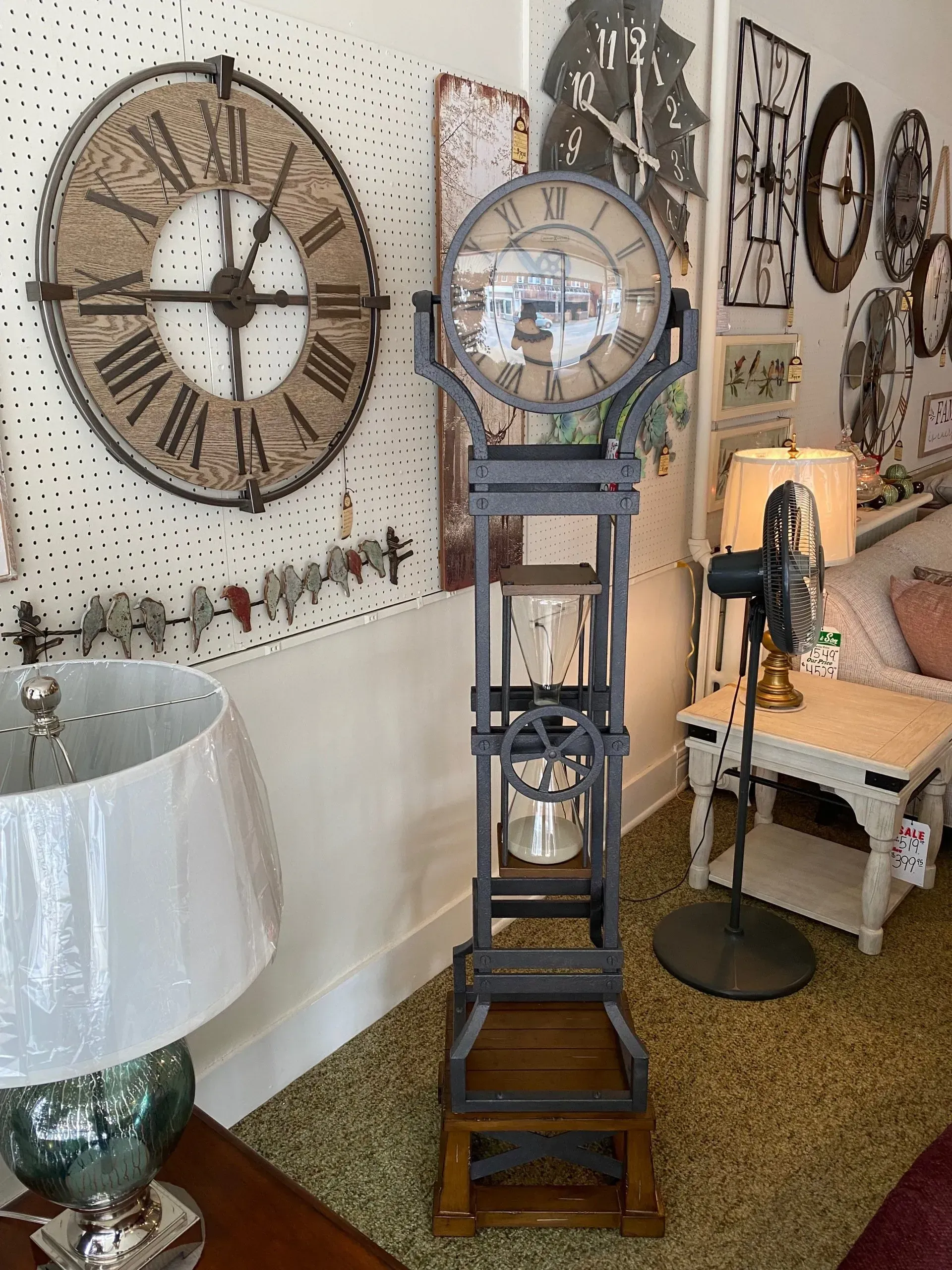 A tall, decorative clock with a round face, wooden frame, and glass jars. It's in a home decor setting.