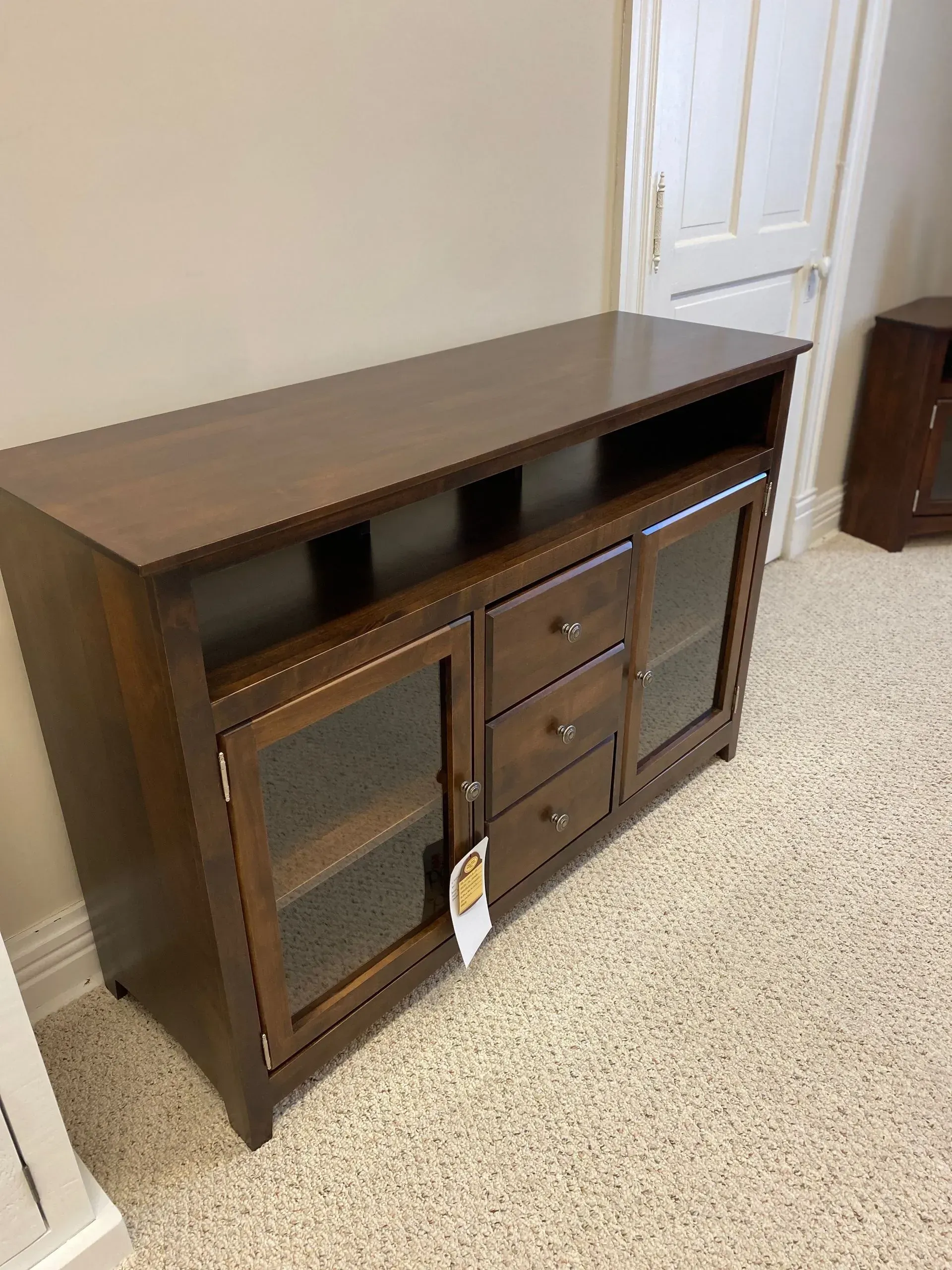Brown wooden TV stand with glass doors and drawers, on a beige carpet.