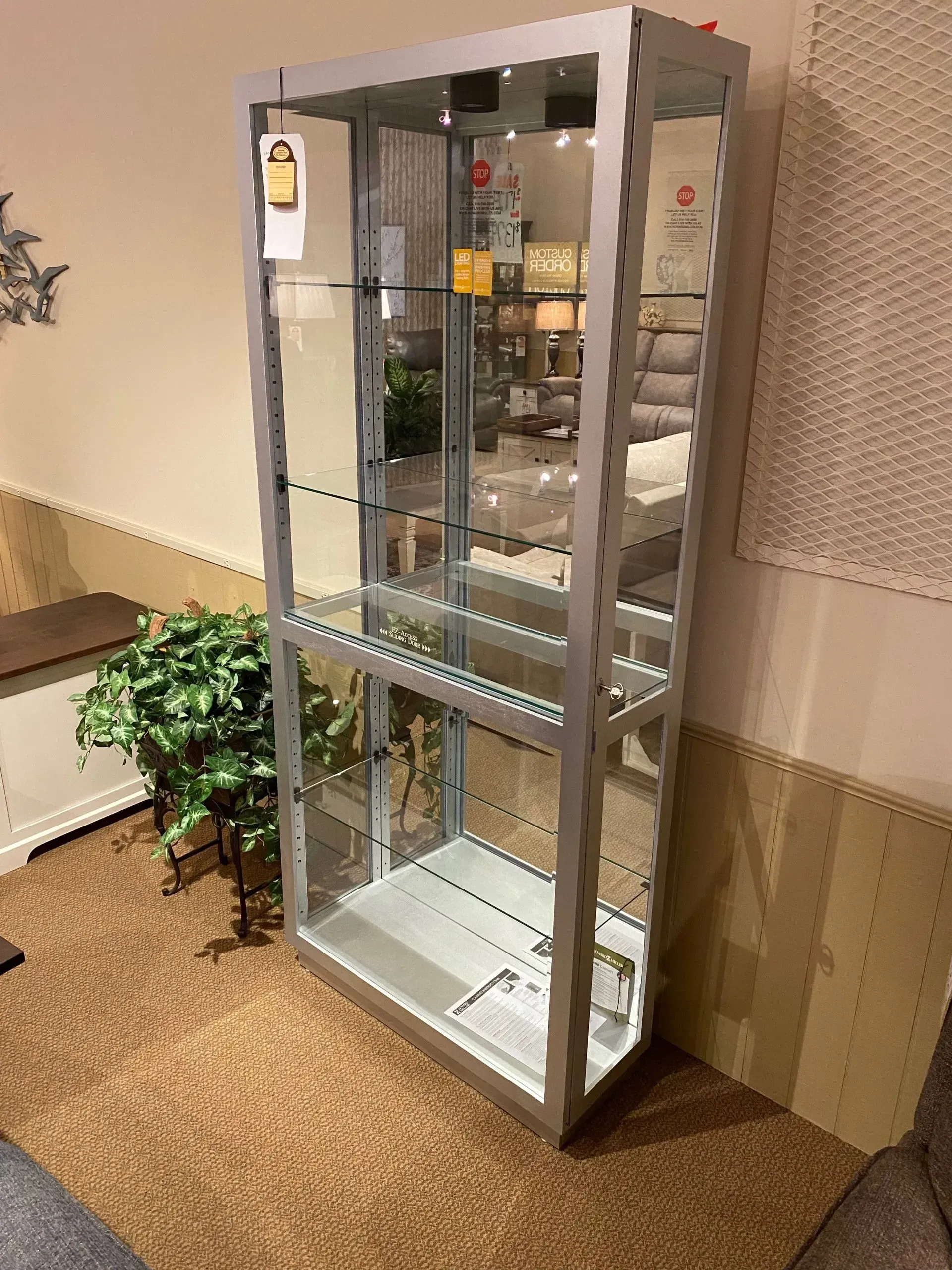 Silver framed glass display cabinet on carpet in a store.