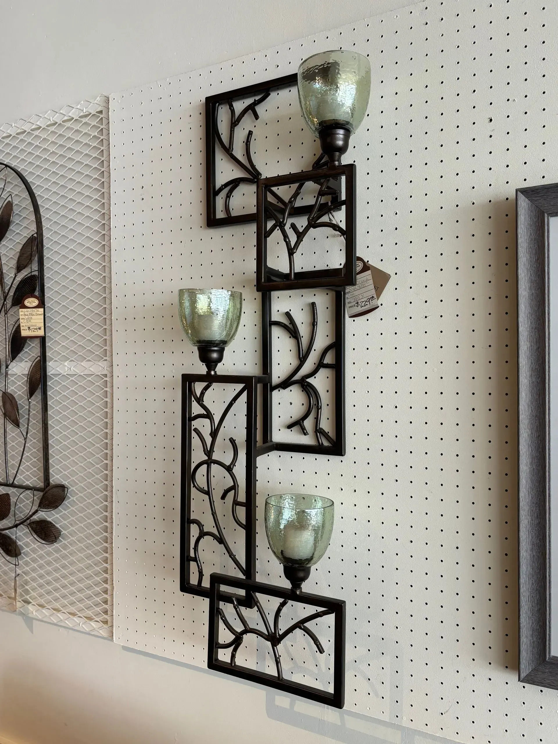 Black metal wall sconce with three glass candle holders on a white wall.