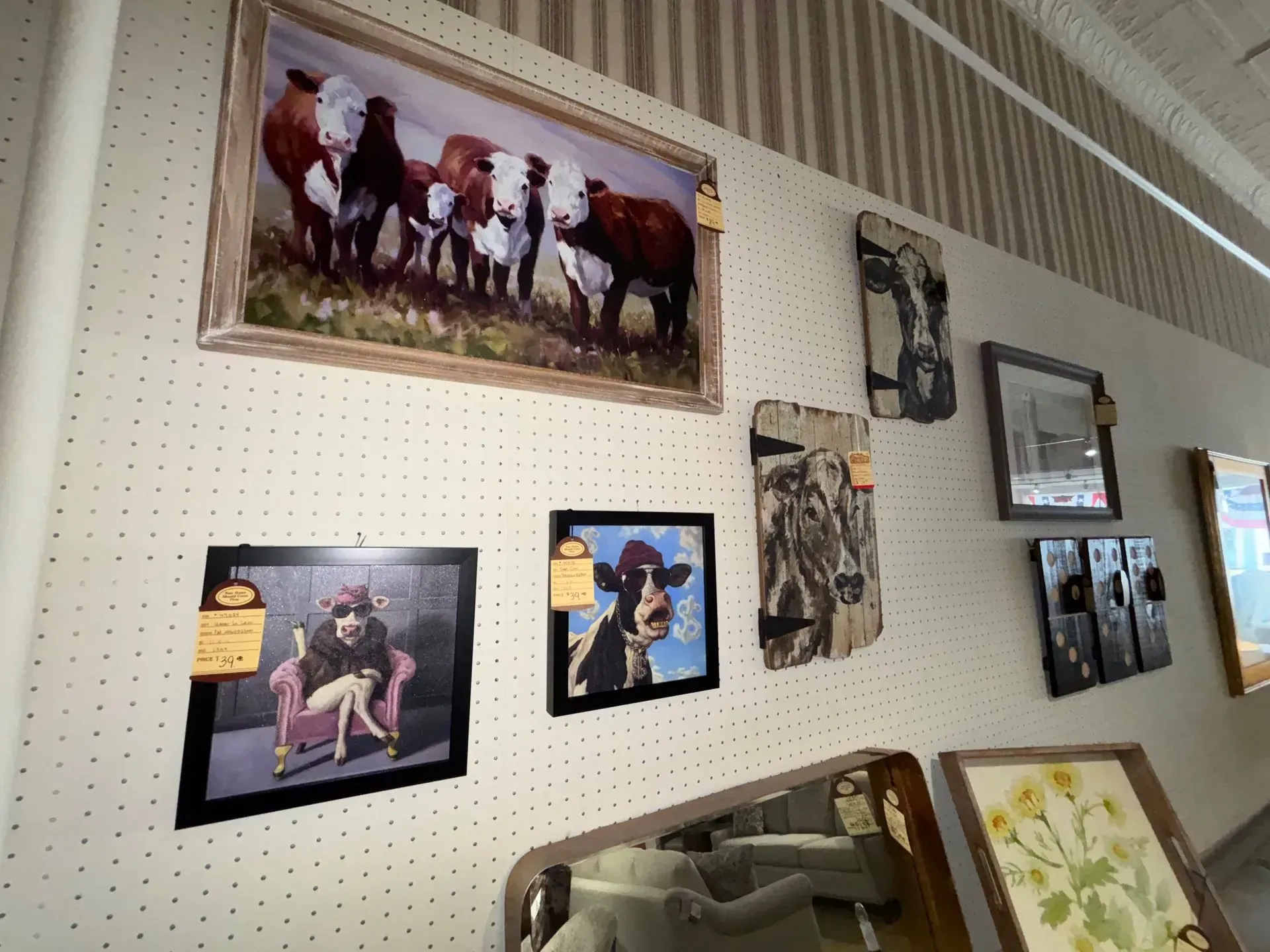 Wall displaying cow-themed art and mirrors with price tags in a store.