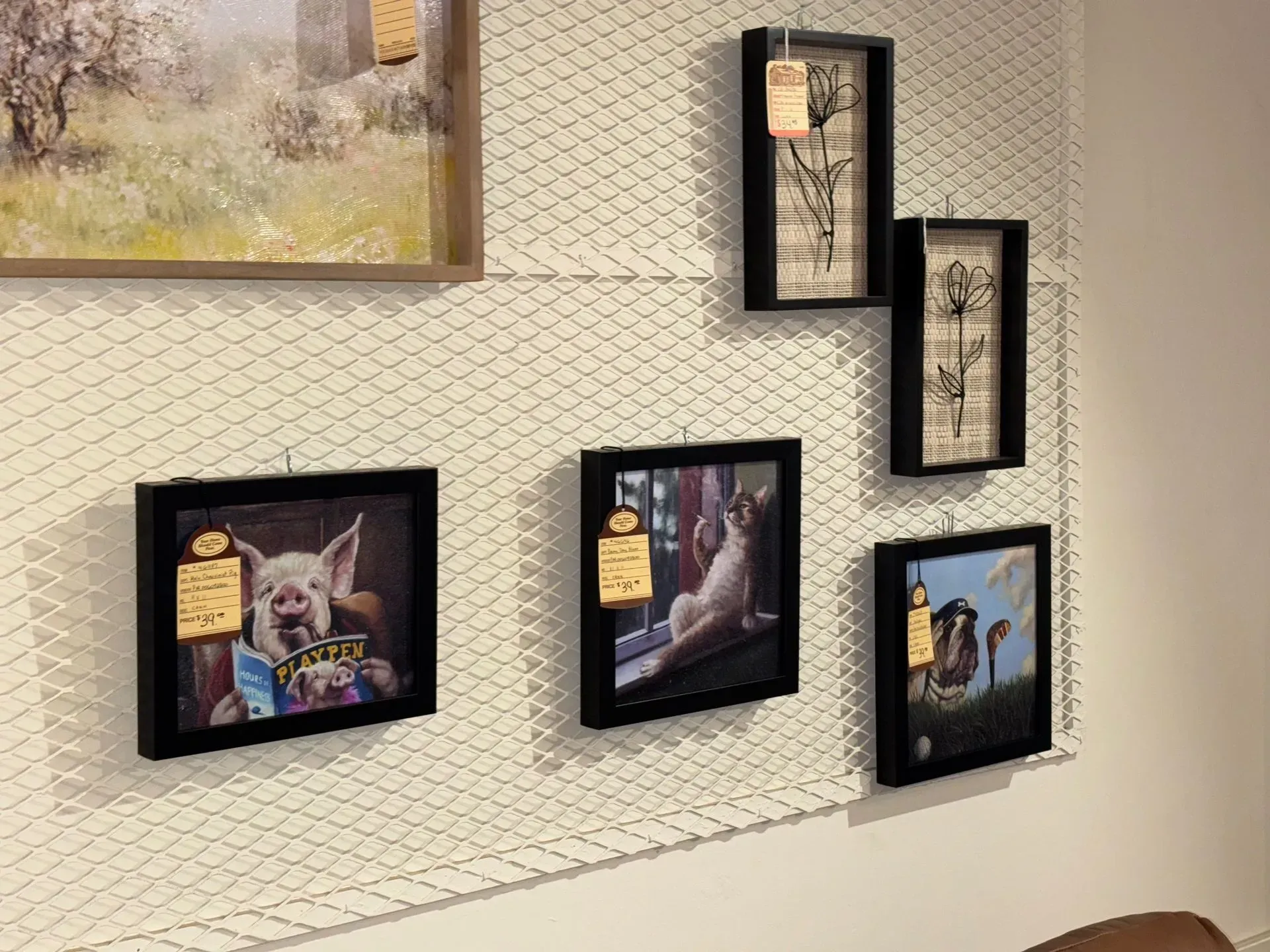 Artwork hanging on a white wall. Paintings include landscapes, a pig reading, and other animals.