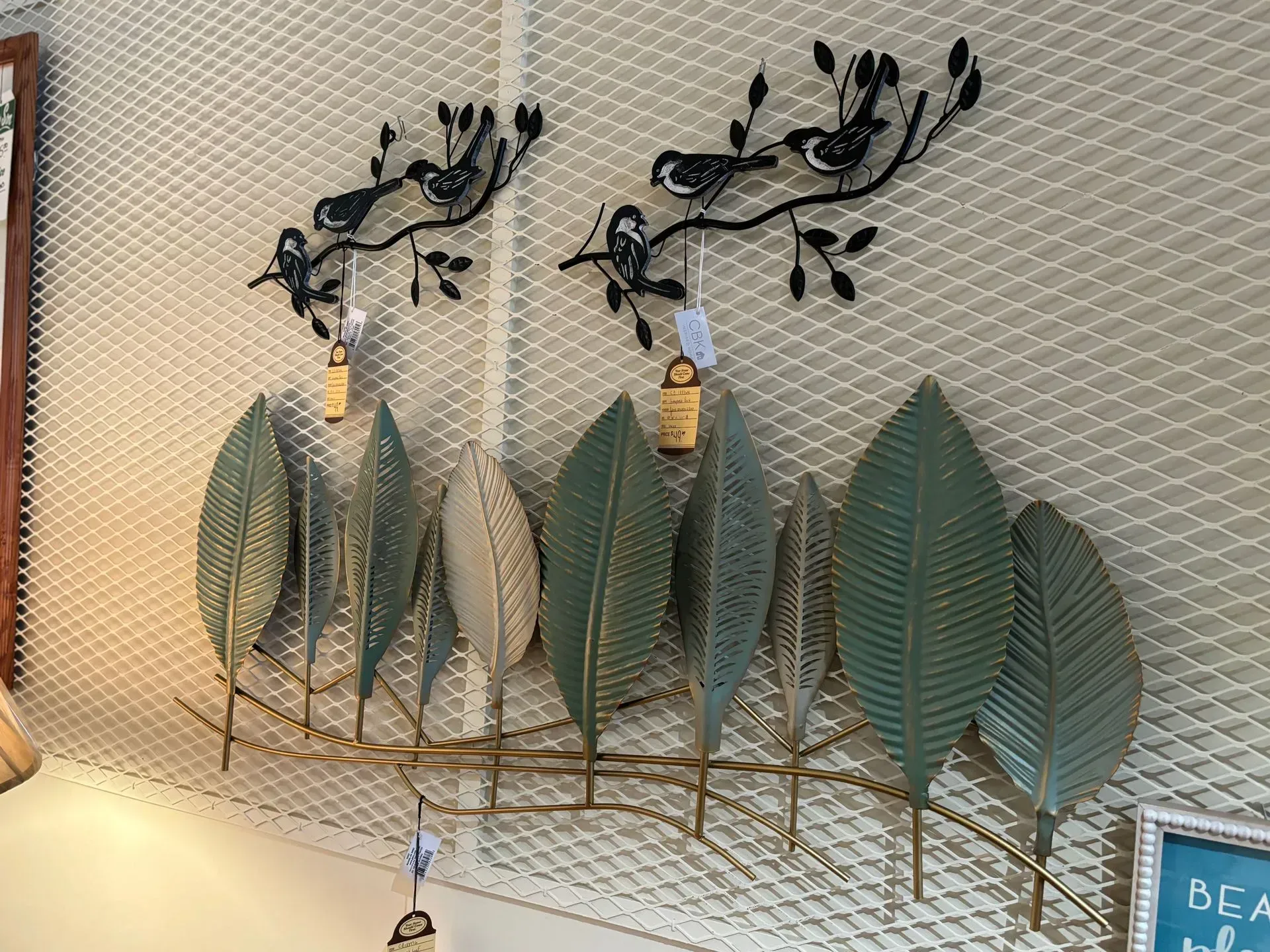 Metal wall art of birds on branches above stylized metal leaves, gold and green against a textured background.