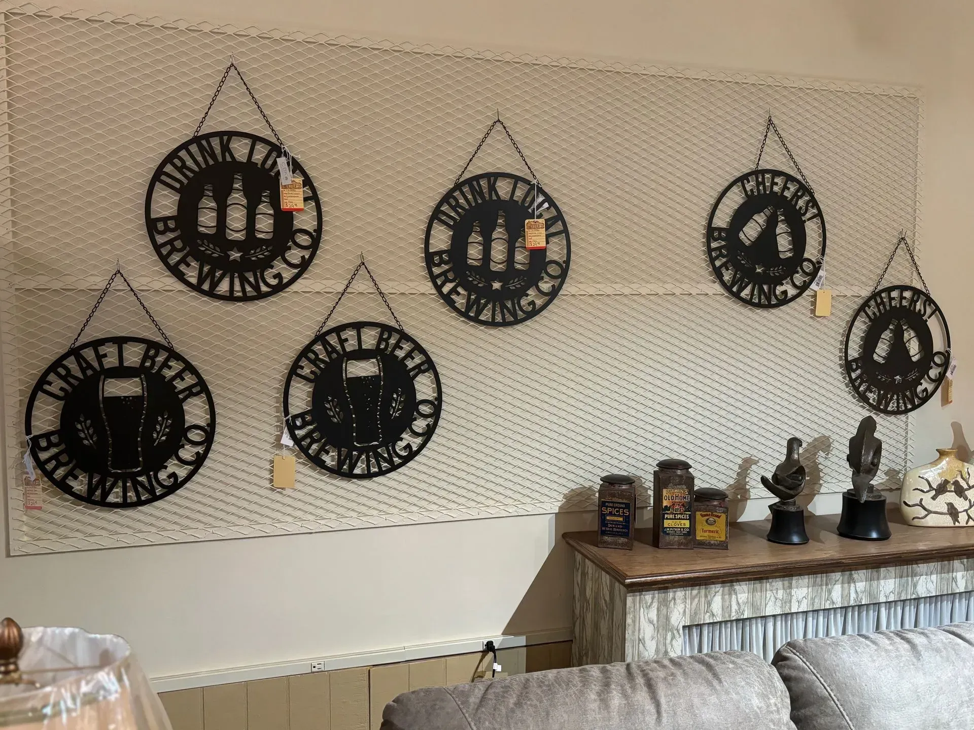 Metal beer signs hang on a pegboard wall. A shelf displays items and a couch sits in front.