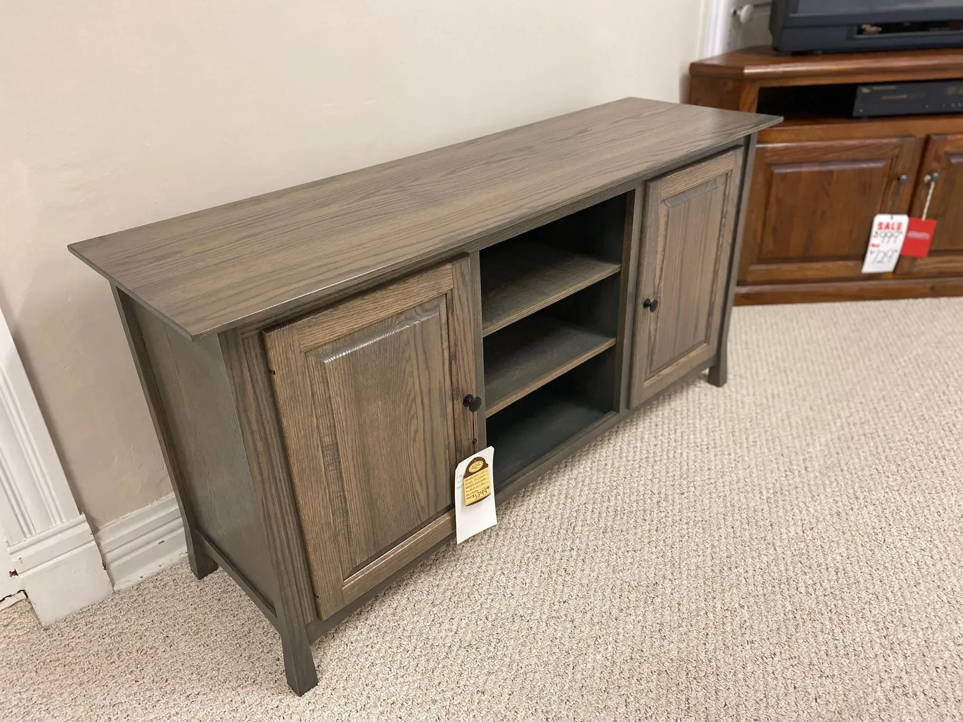Wooden TV console with two doors and open shelving, in a carpeted room.