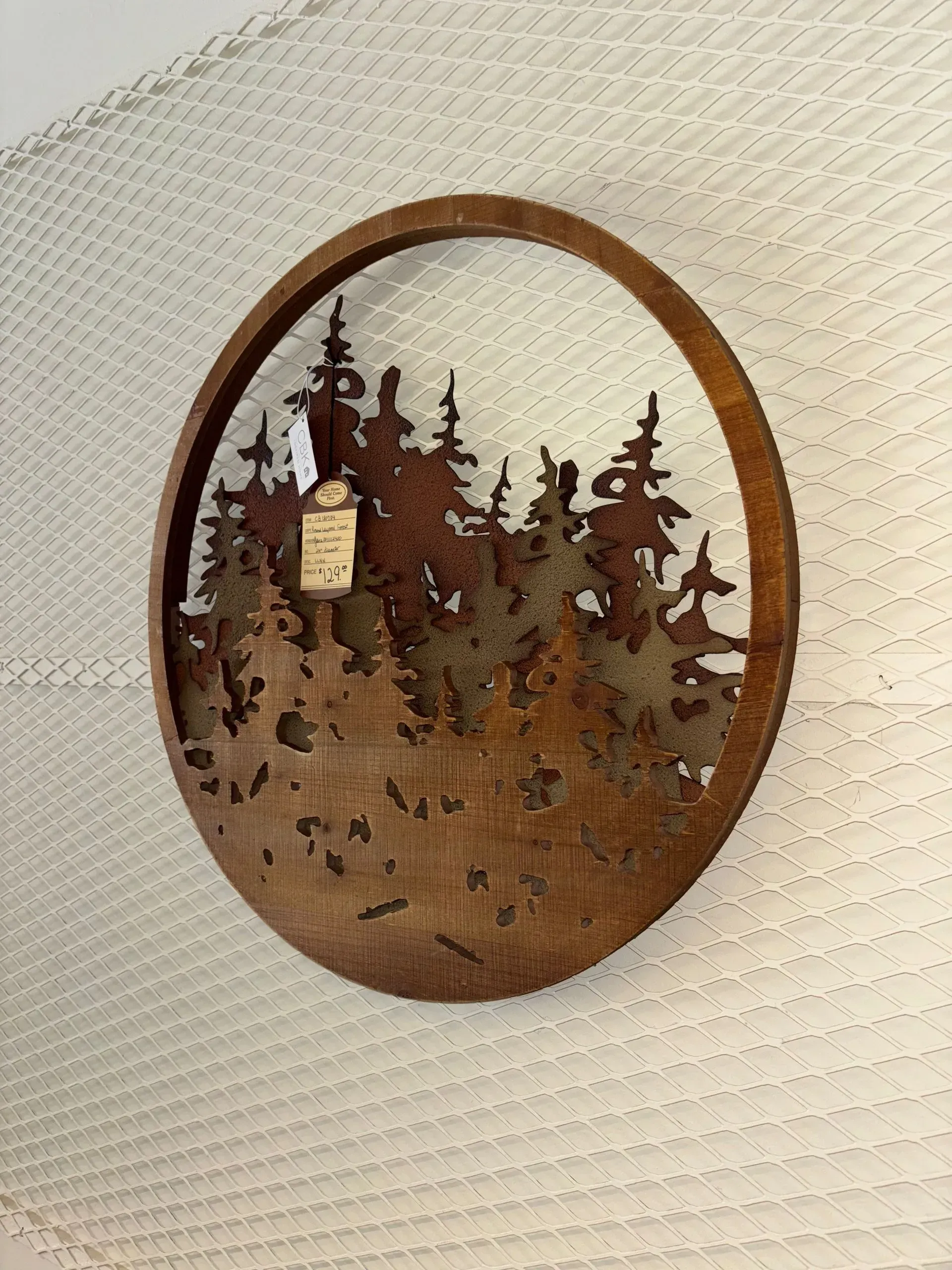 Wooden oval wall art with cutout forest silhouette and small tag.