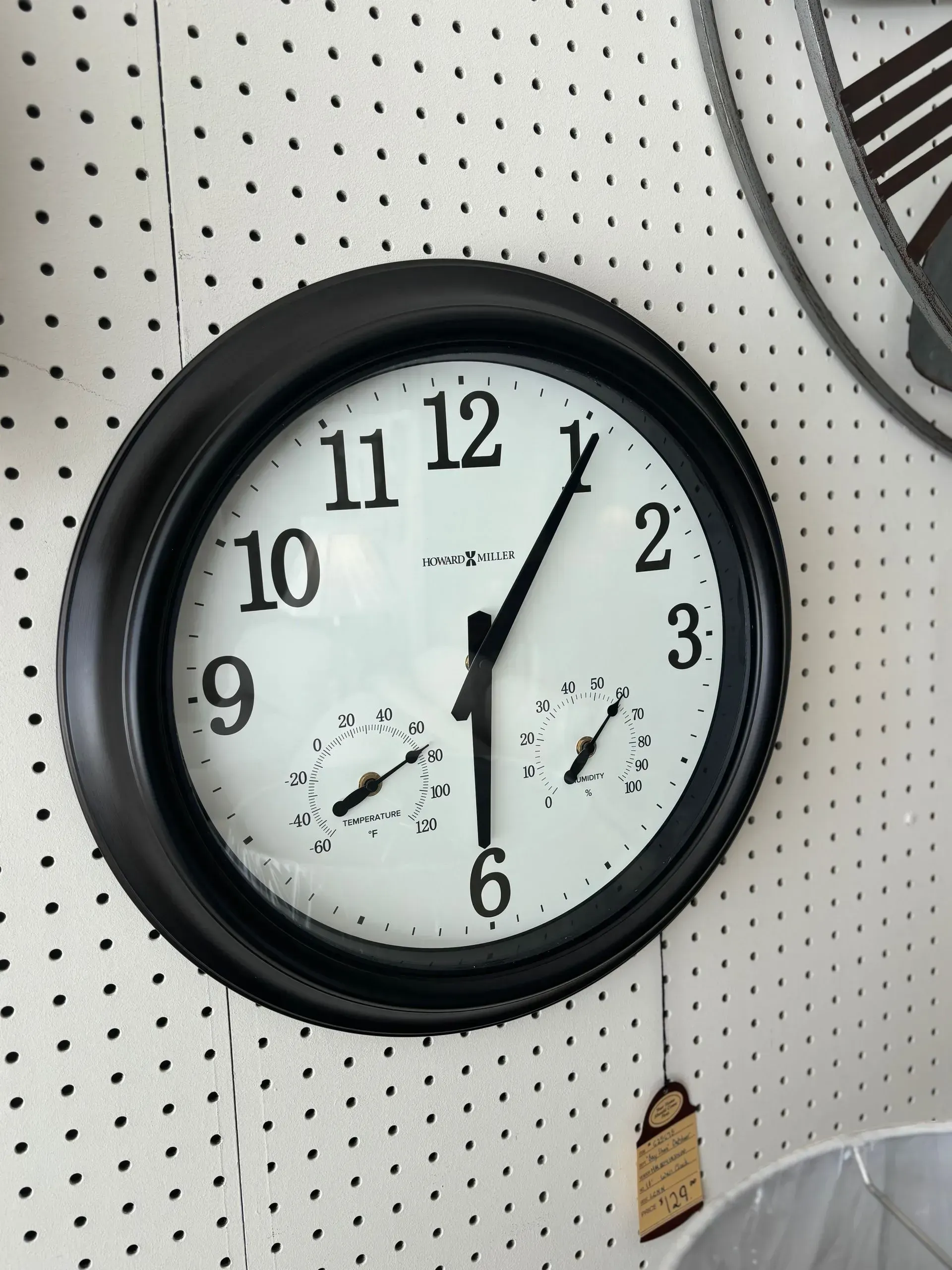 Black-framed clock on a white wall. The clock face is white with black numerals, hands, and two smaller dials.