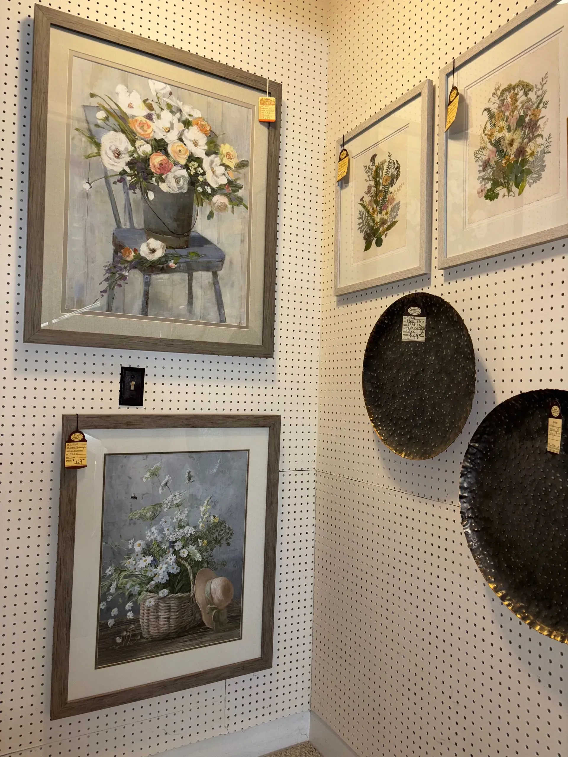 Gallery wall: framed floral art and decorative plates against a white, perforated wall.