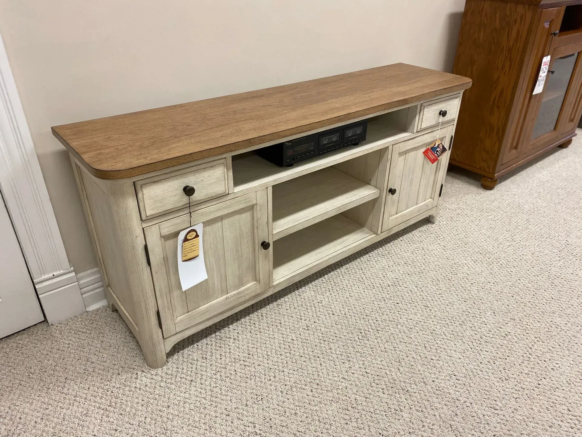 Cream-colored TV console with light brown top; center open shelving, side cabinets, and a drawer. Tag attached.