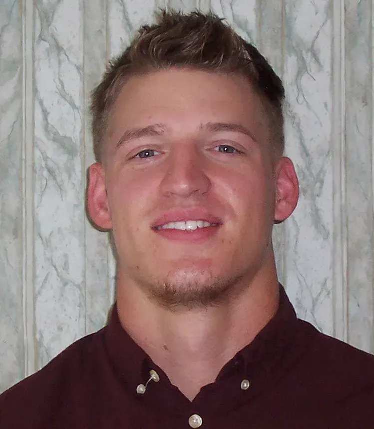 Man with short, light brown hair, smiling, wearing a dark red button-down shirt.