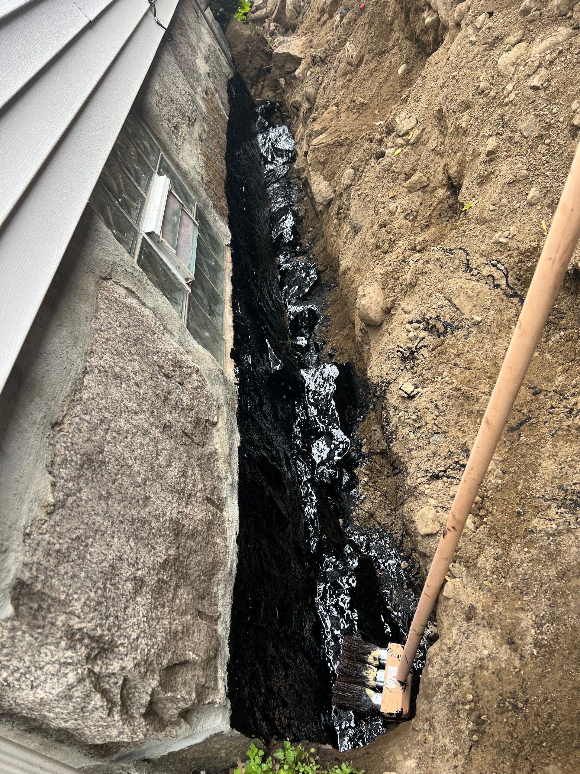 Narrow trench beside a house foundation, with black water or debris running through it.