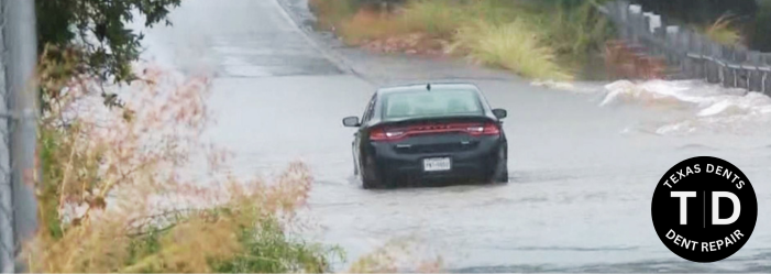 Car driving through floodwater on a San Antonio road during heavy storm conditions, highlighting ris
