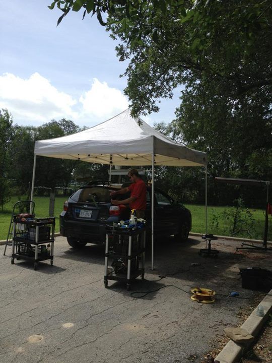 a man is working on a car under a white tent