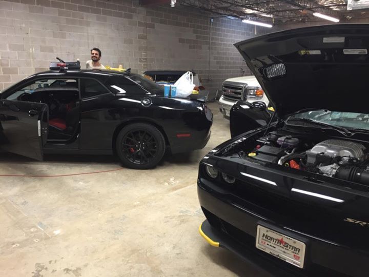 two black cars are parked in a garage with the hood open