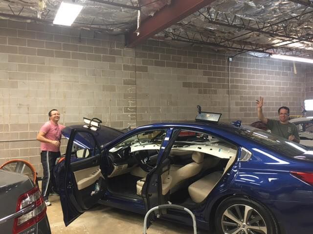 two men are working on a blue car in a garage .