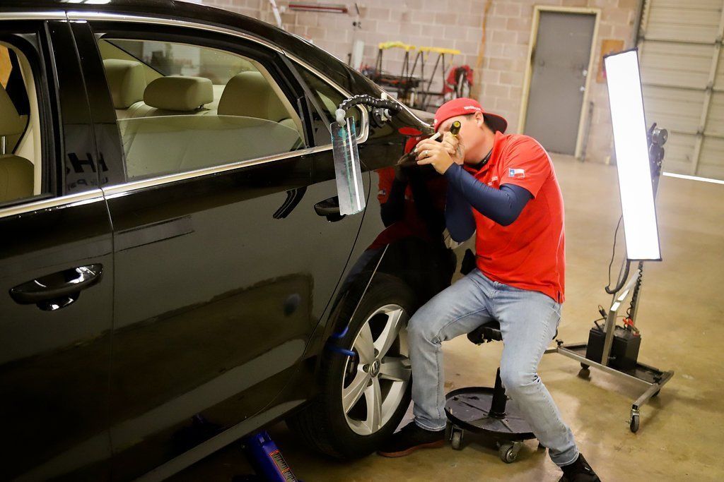 a man is sitting on a stool in front of a black car .