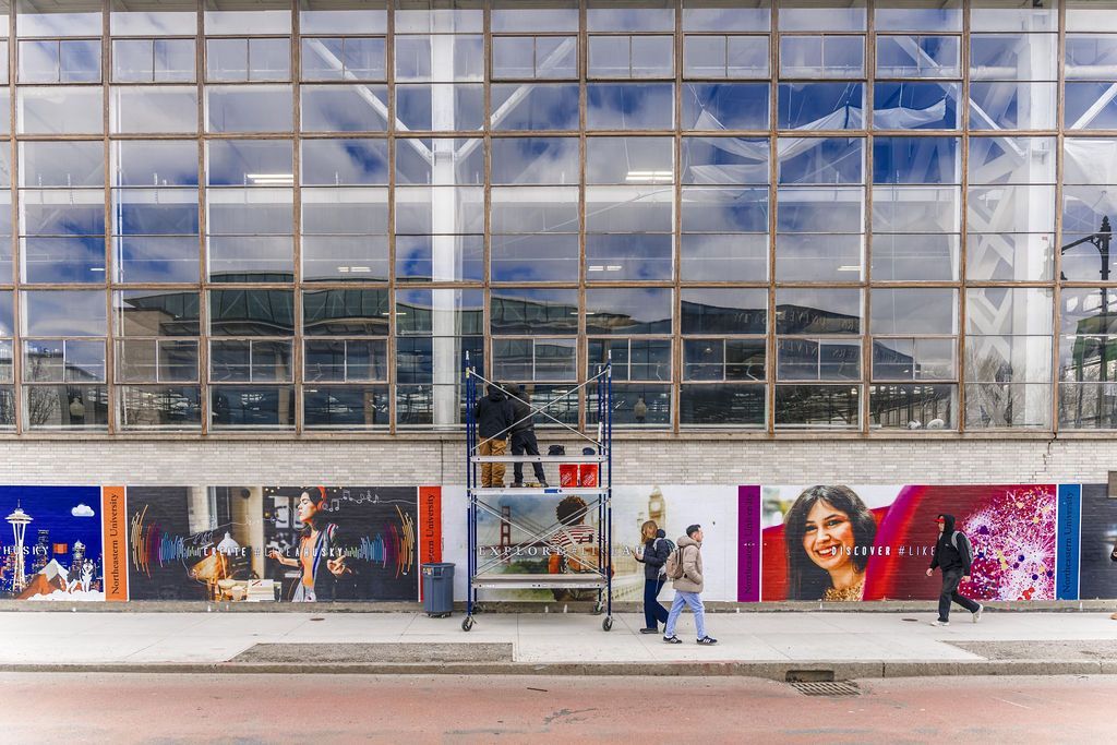Glass-front building with colorful storefront panels and a few pedestrians on the sidewalk