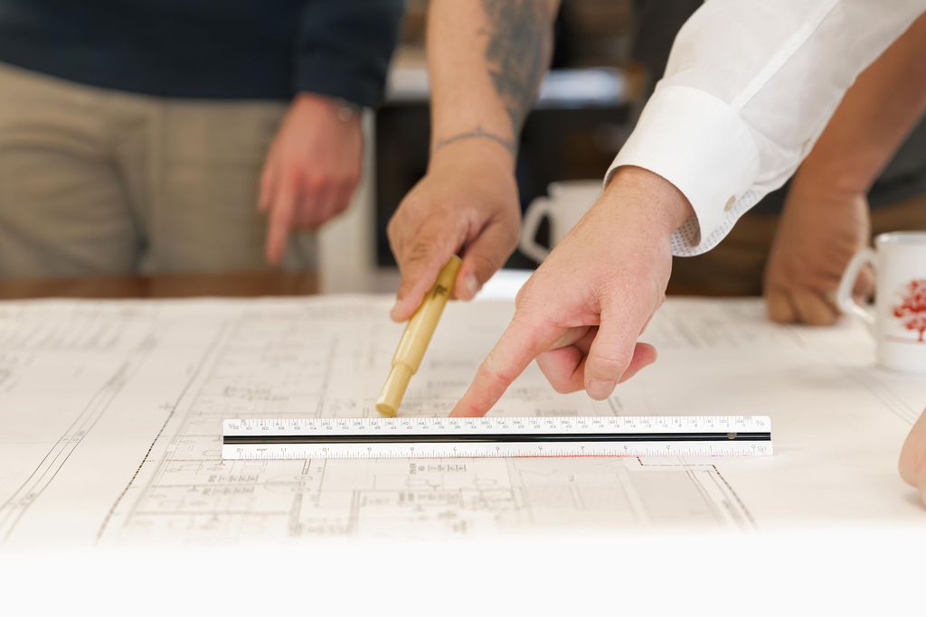 Hands measuring a floor plan with a ruler and pencil on a white drafting table