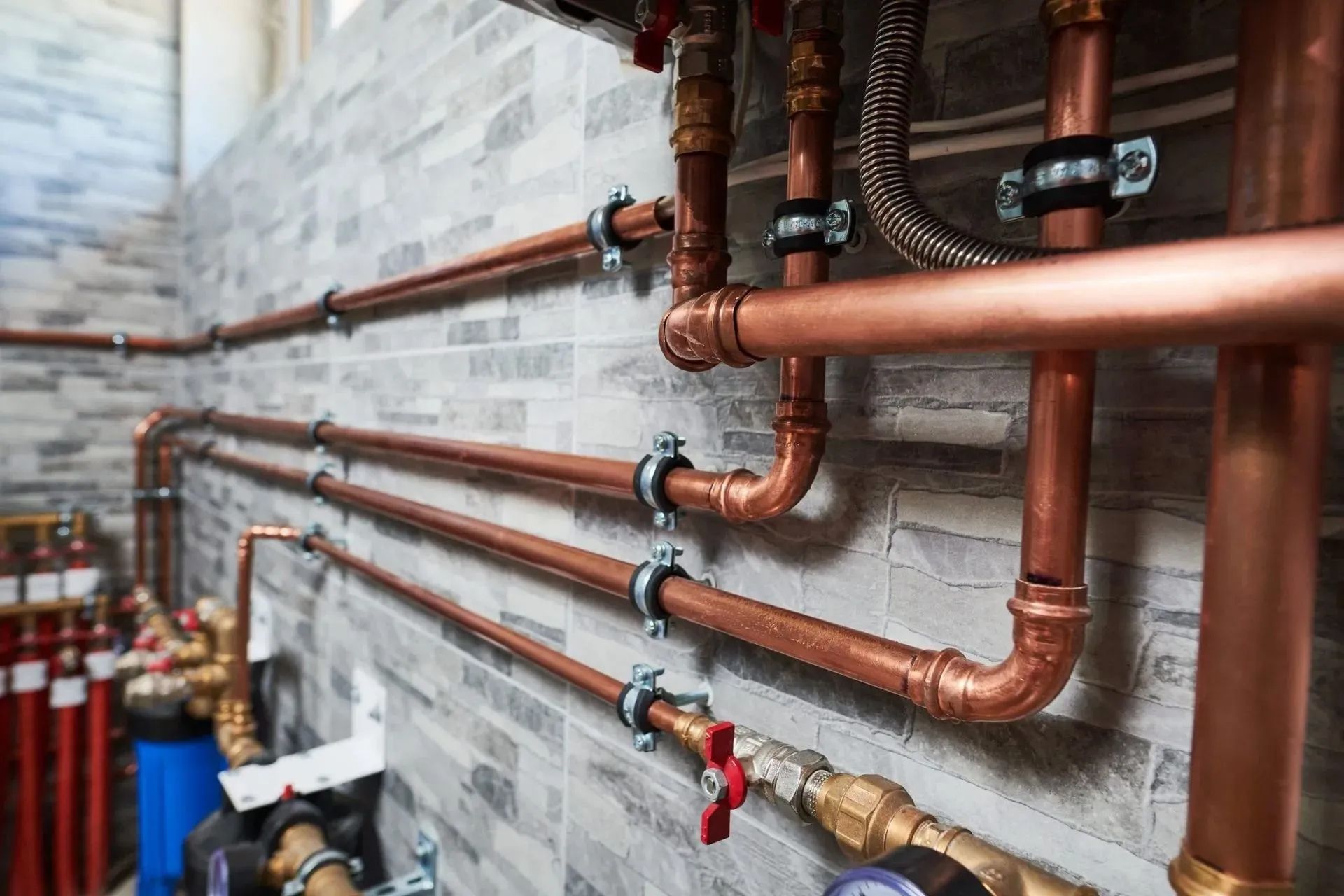 Copper plumbing pipes and valves mounted along a gray brick wall in a utility room