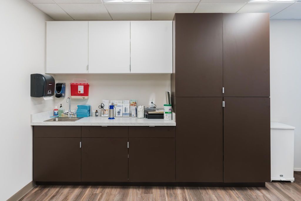 Office kitchenette with dark brown and white cabinets, countertop supplies, and a small trash bin
