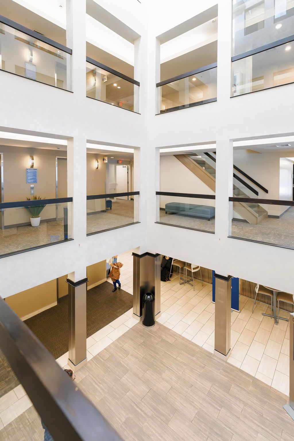 Multi-story atrium with glass-walled walkways, beige floors, and staircase railings surrounding a central open space