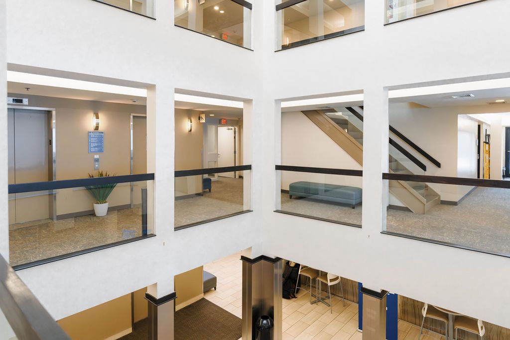 Multi-story office atrium with glass railings, beige walls, and blue seating areas around an open central space