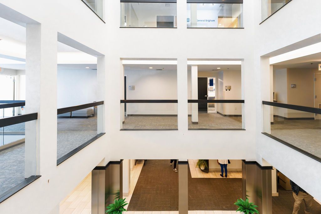 Bright, multi-story atrium with white walls, glass railings, and a few people on the ground floor