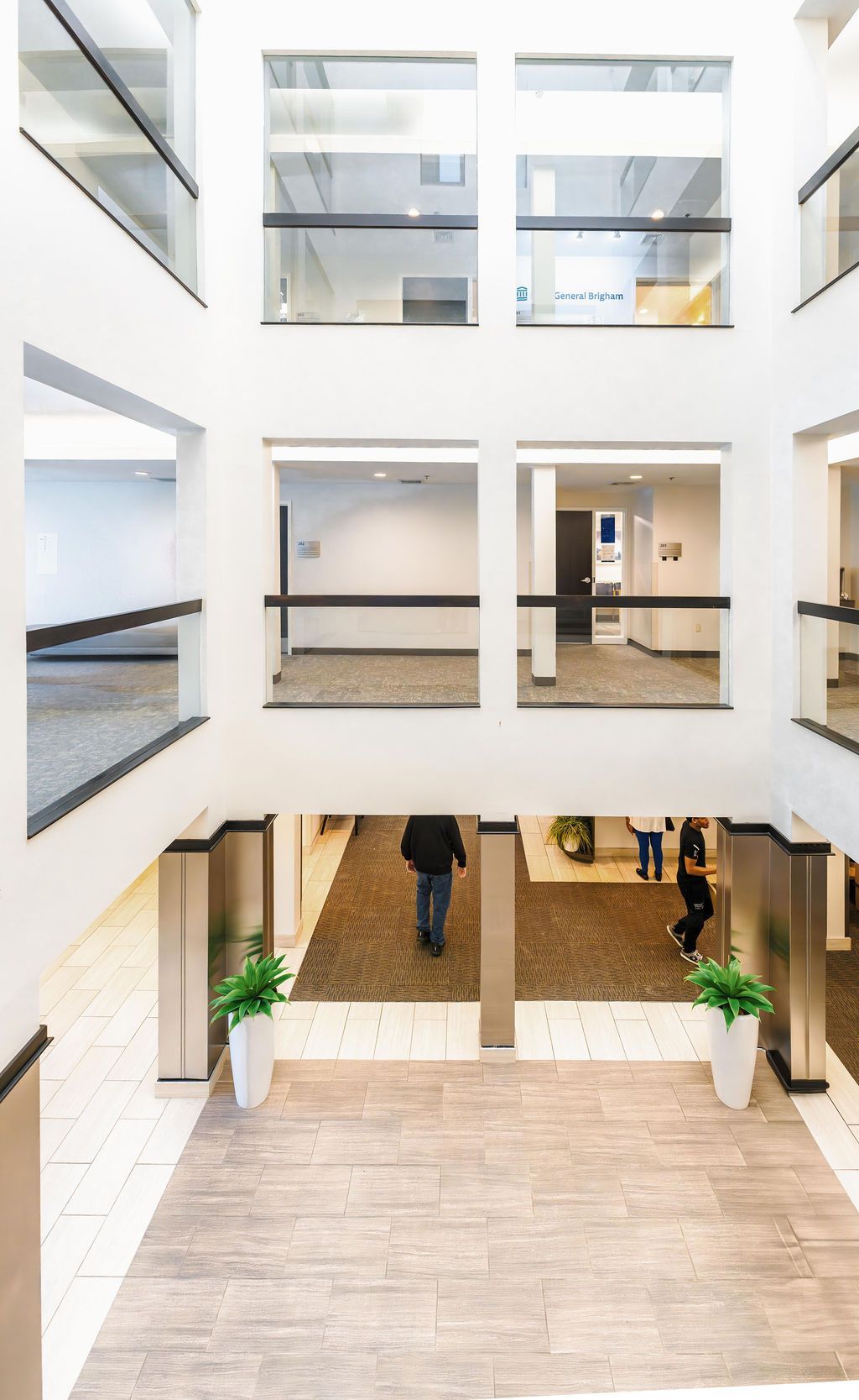 Bright atrium with multiple floors, glass railings, and a central staircase leading to a lobby below.