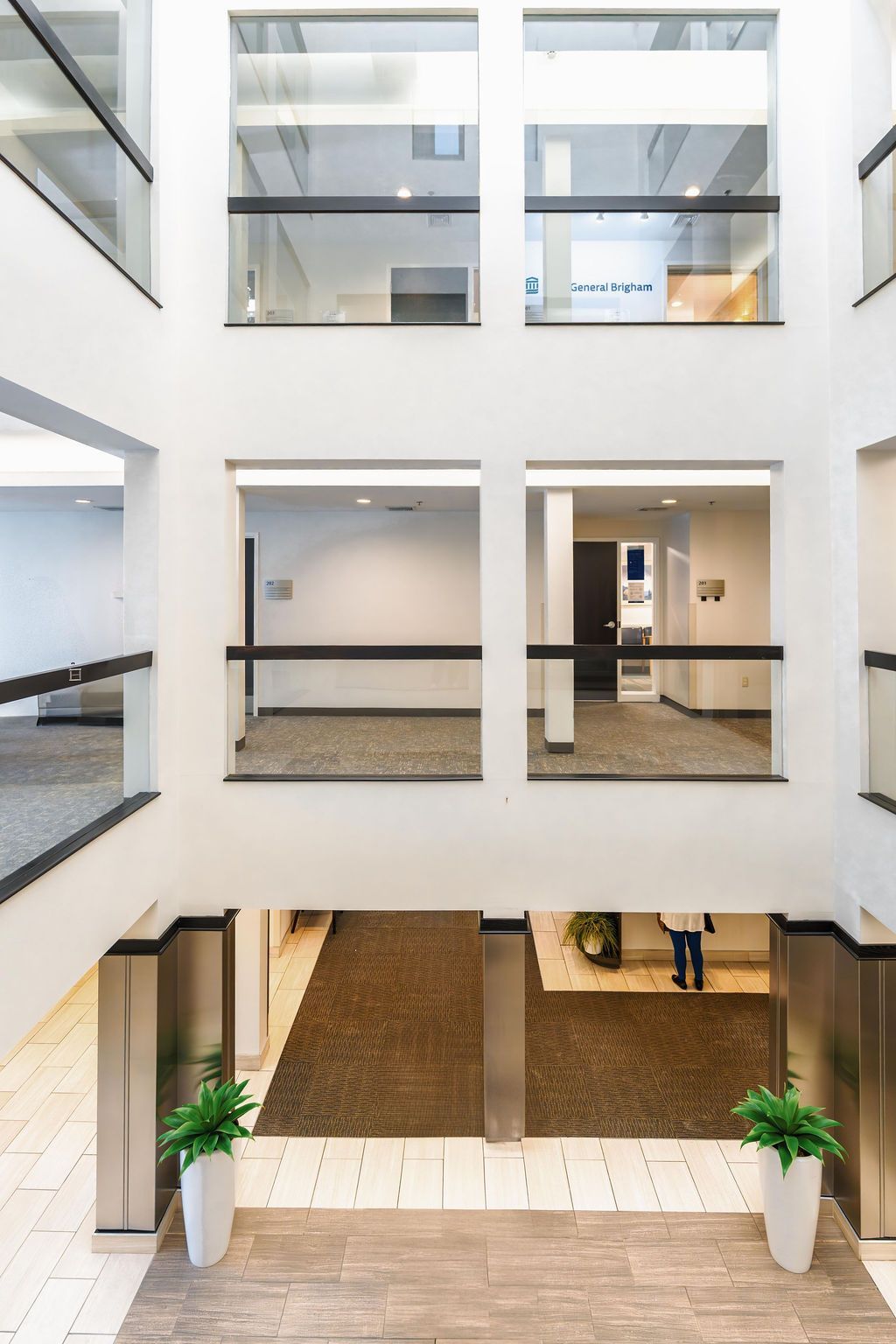Atrium in a modern building with glass-walled offices and a central staircase below.