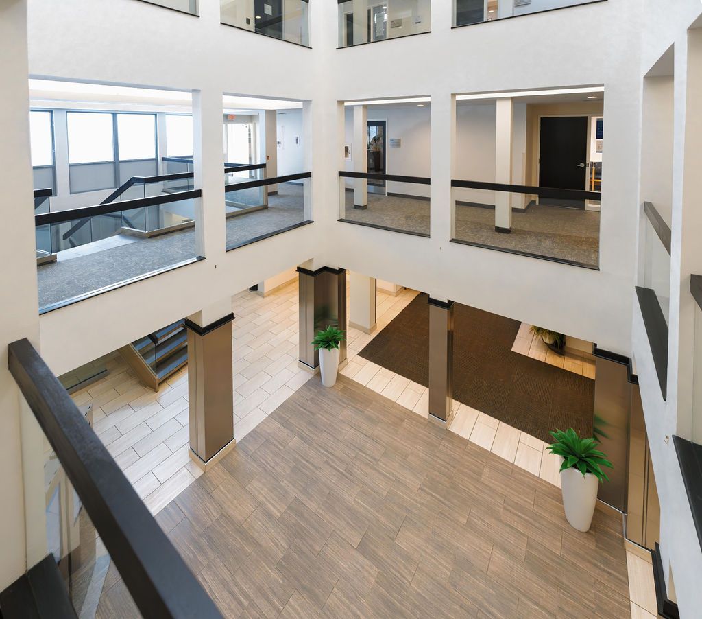 Bright modern office atrium with white walls, glass railings, wood flooring, and potted plants