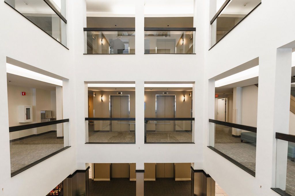 Bright atrium with white walls, glass railings, and multiple floors overlooking a central open space