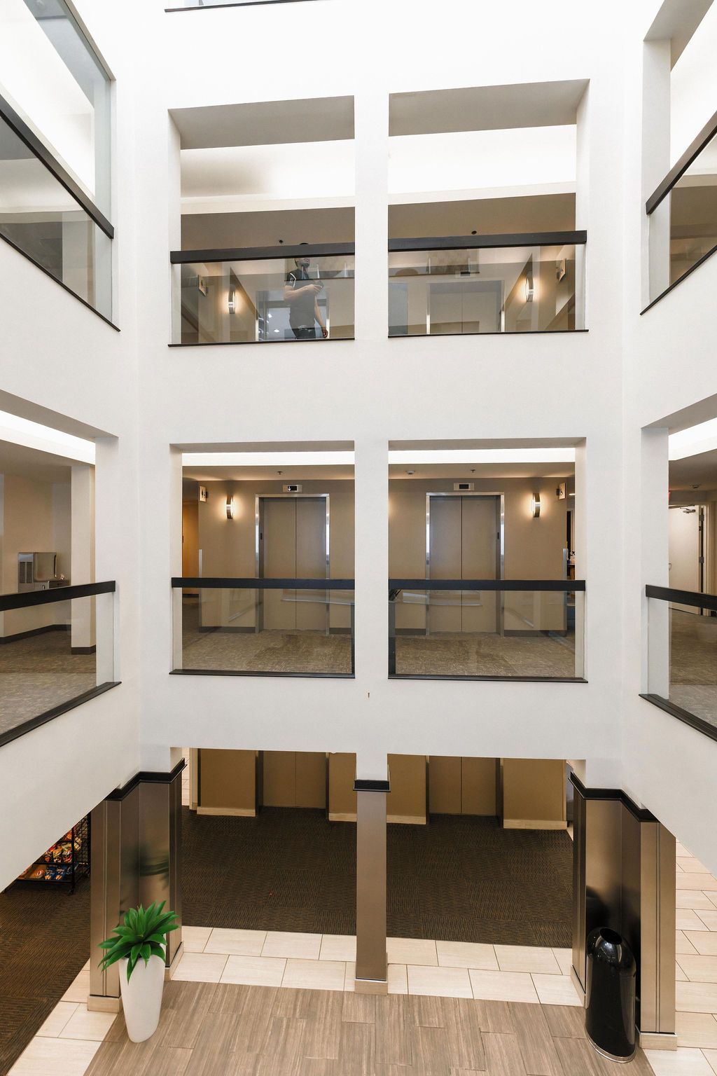 Interior atrium of a modern building with white walls, balconies, and tiled floors, viewed from above