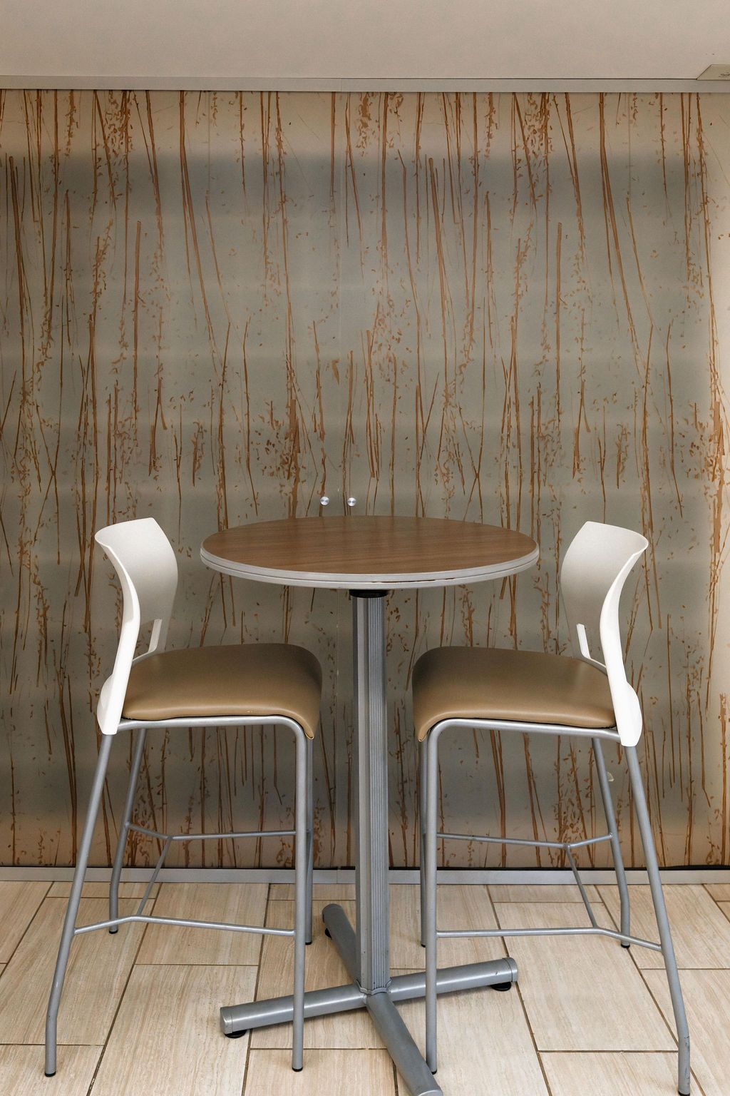 Small café table with two white bar stools against a wood-paneled wall