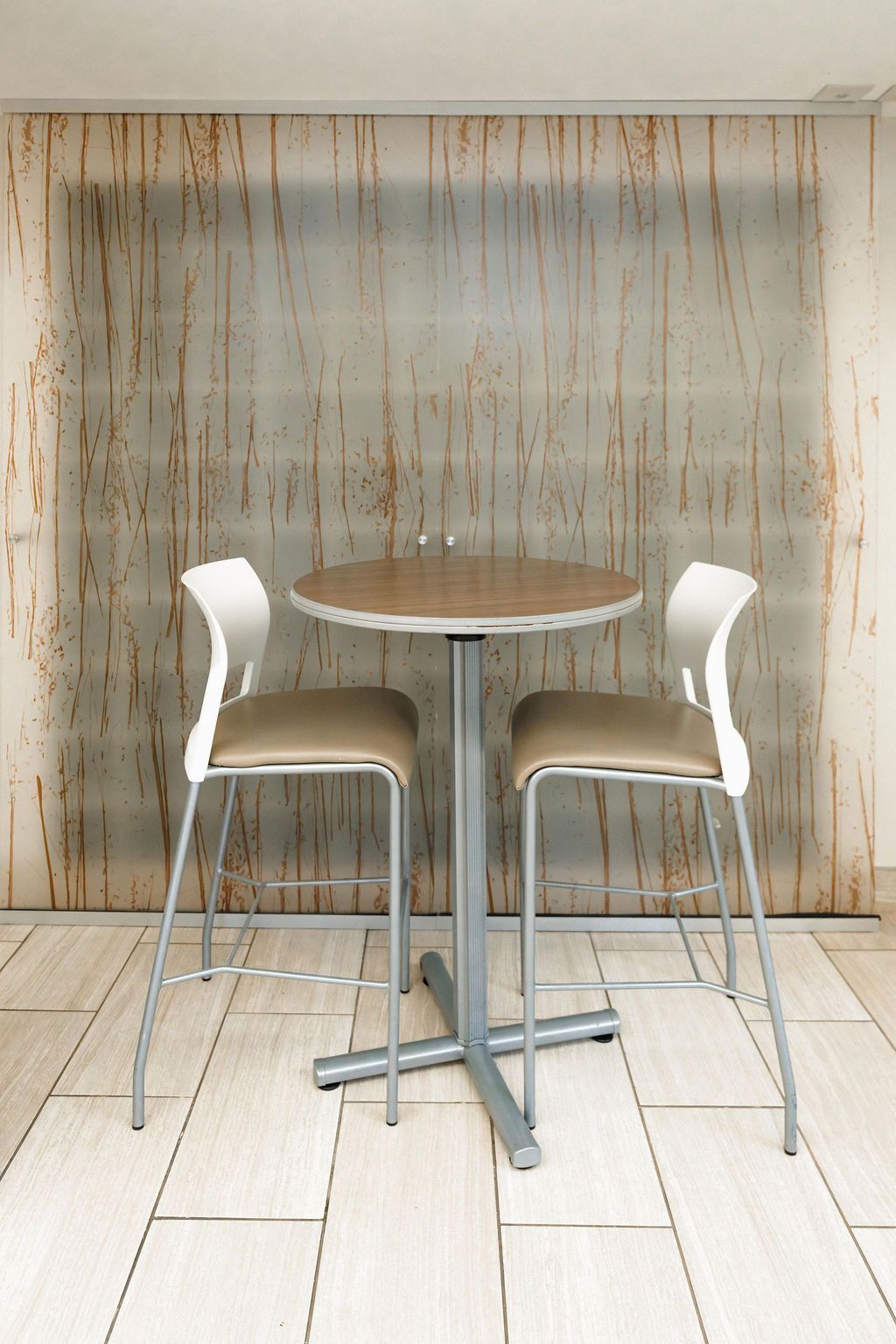 Small round café table with two white bar stools against a textured wall.