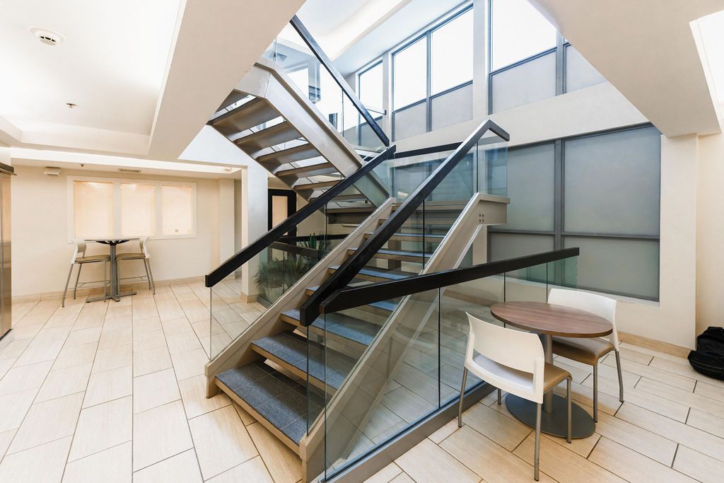Modern office lobby with glass staircase, tiled floor, and small seating area