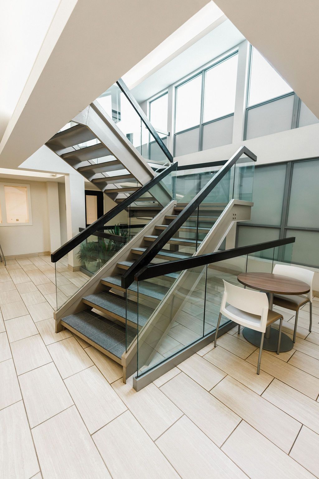 Modern indoor staircase with glass railings and white tiled floor in a bright atrium