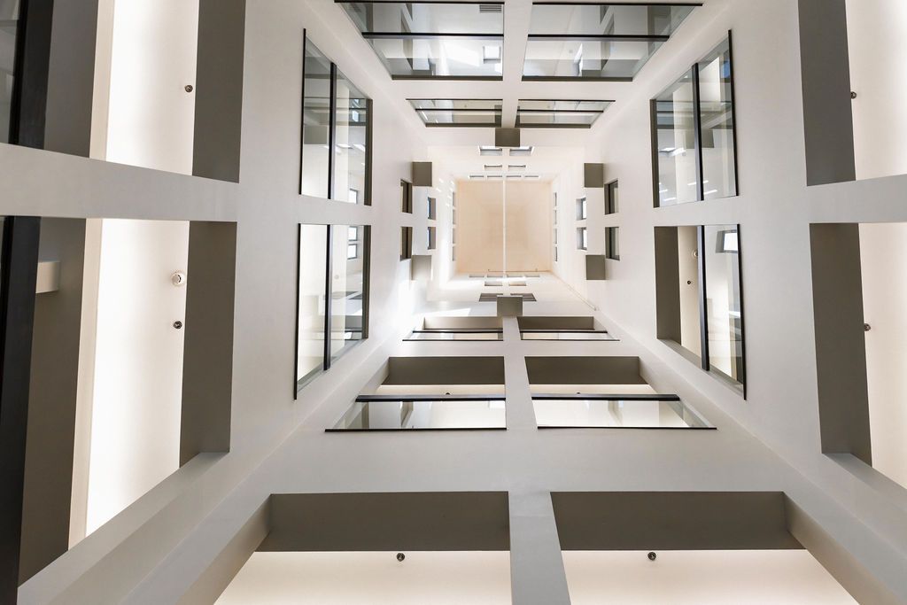 Interior view of a modern atrium with white beams, tall windows, and a skylight above.