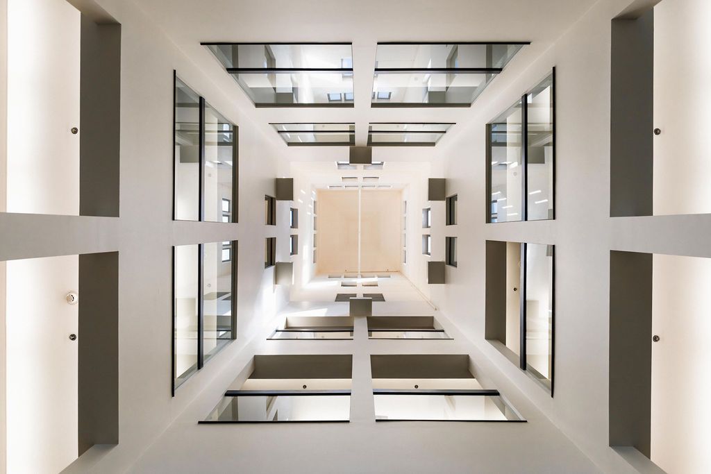Symmetrical white atrium with skylights, glass railings, and a central beige wall panel.