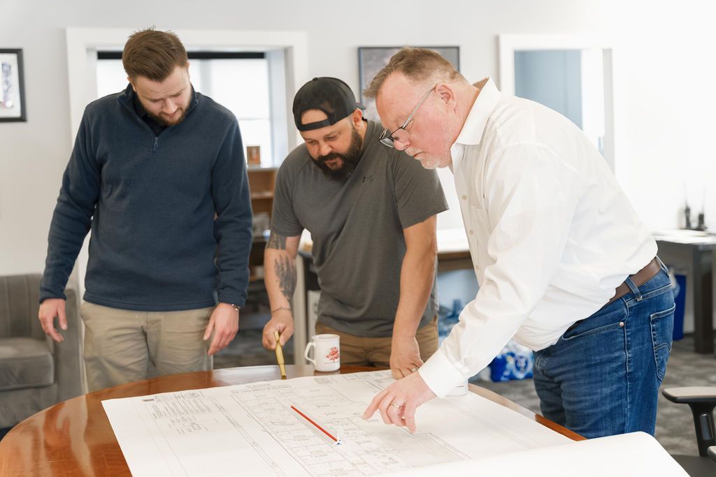 Three people reviewing blueprints around a table in a bright office