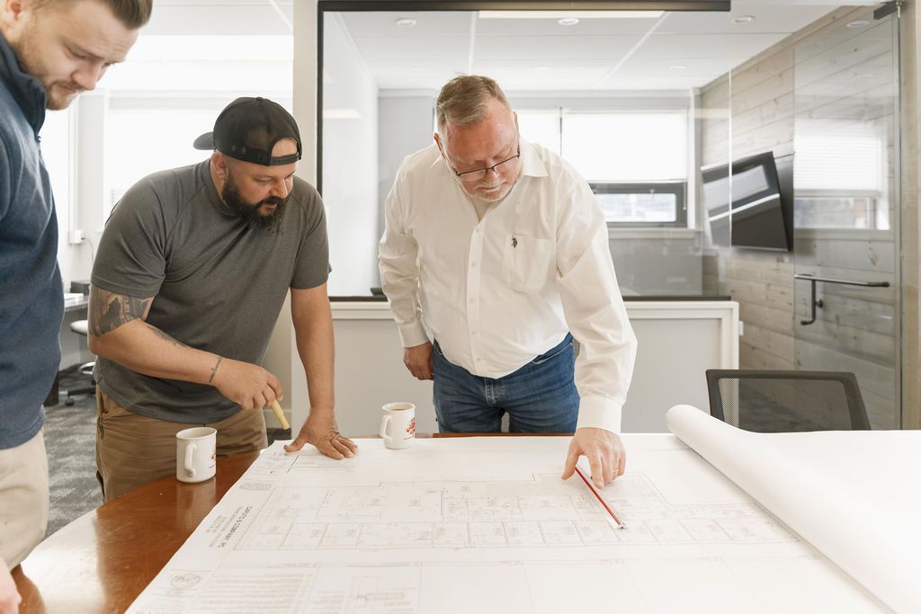 Three people reviewing a large blueprint in a bright office conference room.
