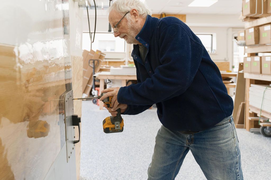 Man in a workshop using a power drill on a wall panel
