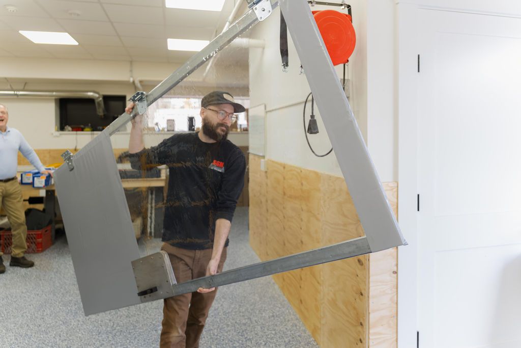 Man carrying a large framed panel through an office hallway, with desks and chairs in the background
