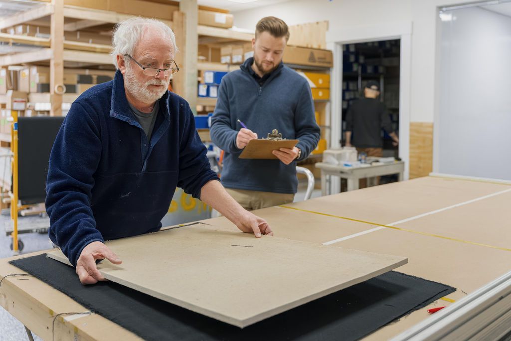 Two people working in a workshop, lifting a large flat board from a table.