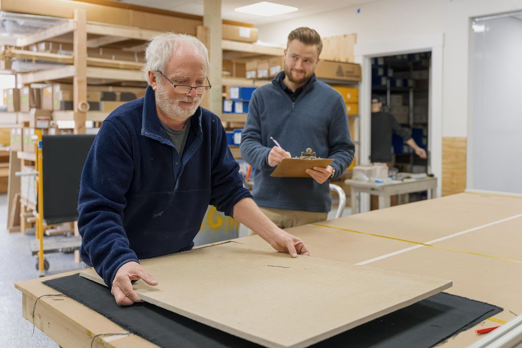 Two workers in a workshop carrying a large wooden panel on a table saw