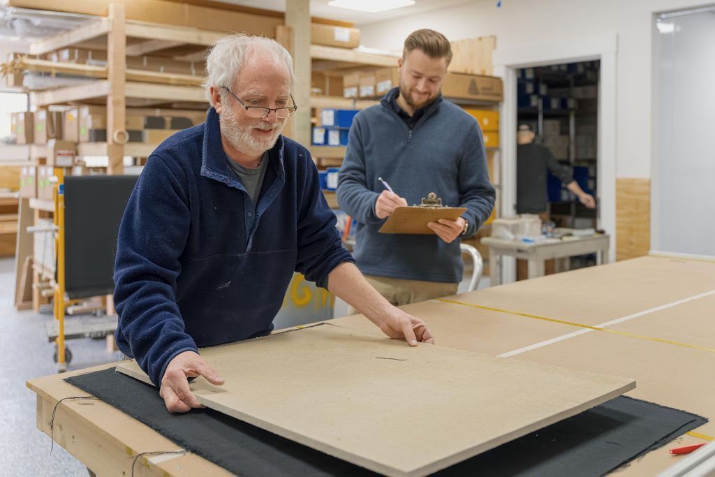 Two workers measuring a large board in a woodworking shop