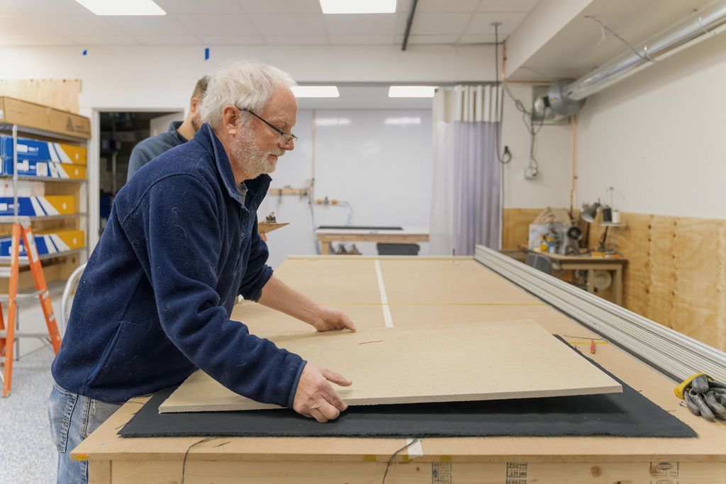 Man working with large cardboard sheet on a workbench in a workshop