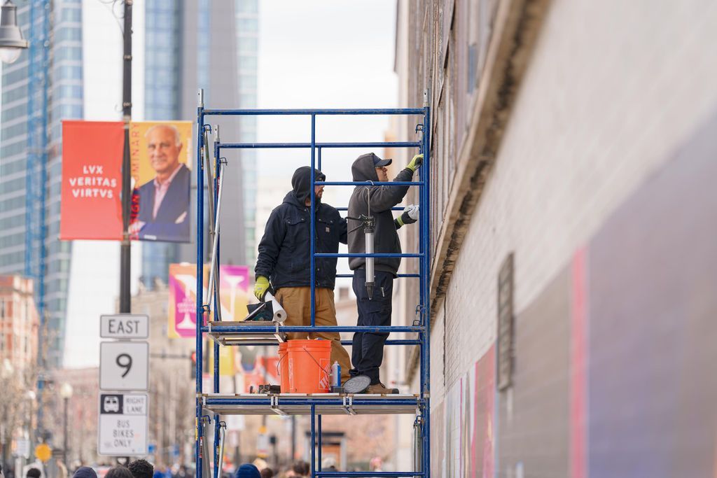 Workers on a blue lift painting a tall mural on a city building wall