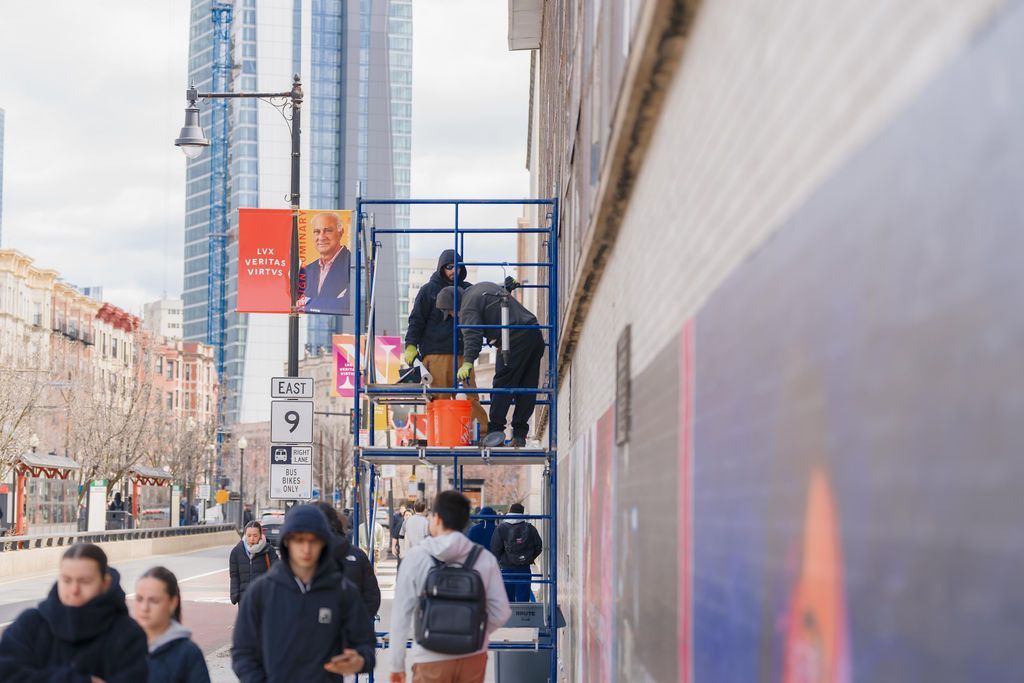 Pedestrians on a city sidewalk beside scaffolding and a building mural on a winter day